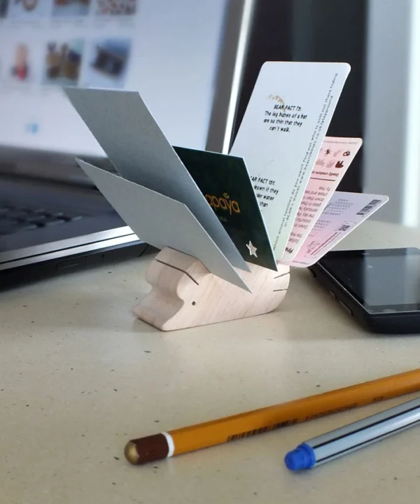 S dydžio medinis darbo stalo organizatorius ežiukas su sudėtomis kortelėmis, stovintis šalia nešiojamojo kompiuterio ir pieštukų