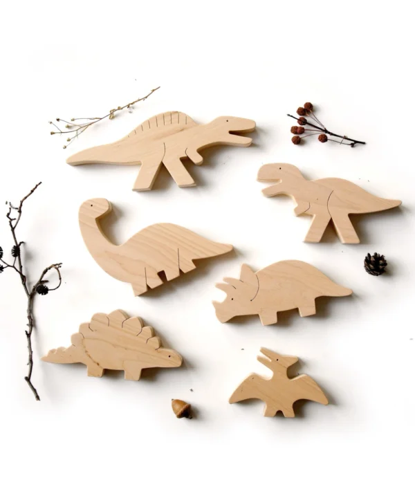 Estetiškas 6 medinių dinozaurų rinkinys išdėliotas šalia kankorėžių ir šakelių – natūralus Montessori žaislas vaikams.