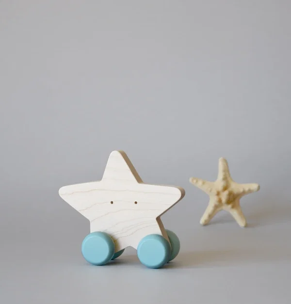 Rankų darbo medinis stumdomas žvaigždės formos žaislas su šviesiai mėlynais ratukais ant neutralaus fono, minimalistinis vaikų žaislas