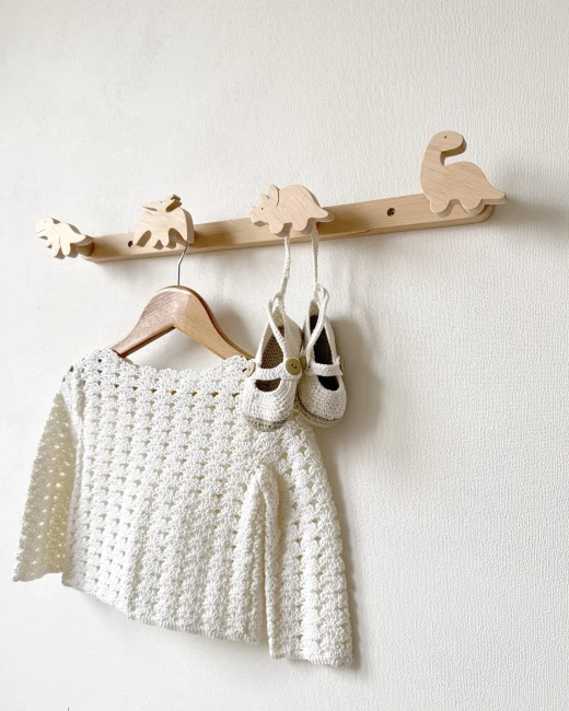 Rankų darbo medinė kabykla su keturiais dinozaurais, nufotografuota kampu, su kabančiu nertu megztuku ir batukais.