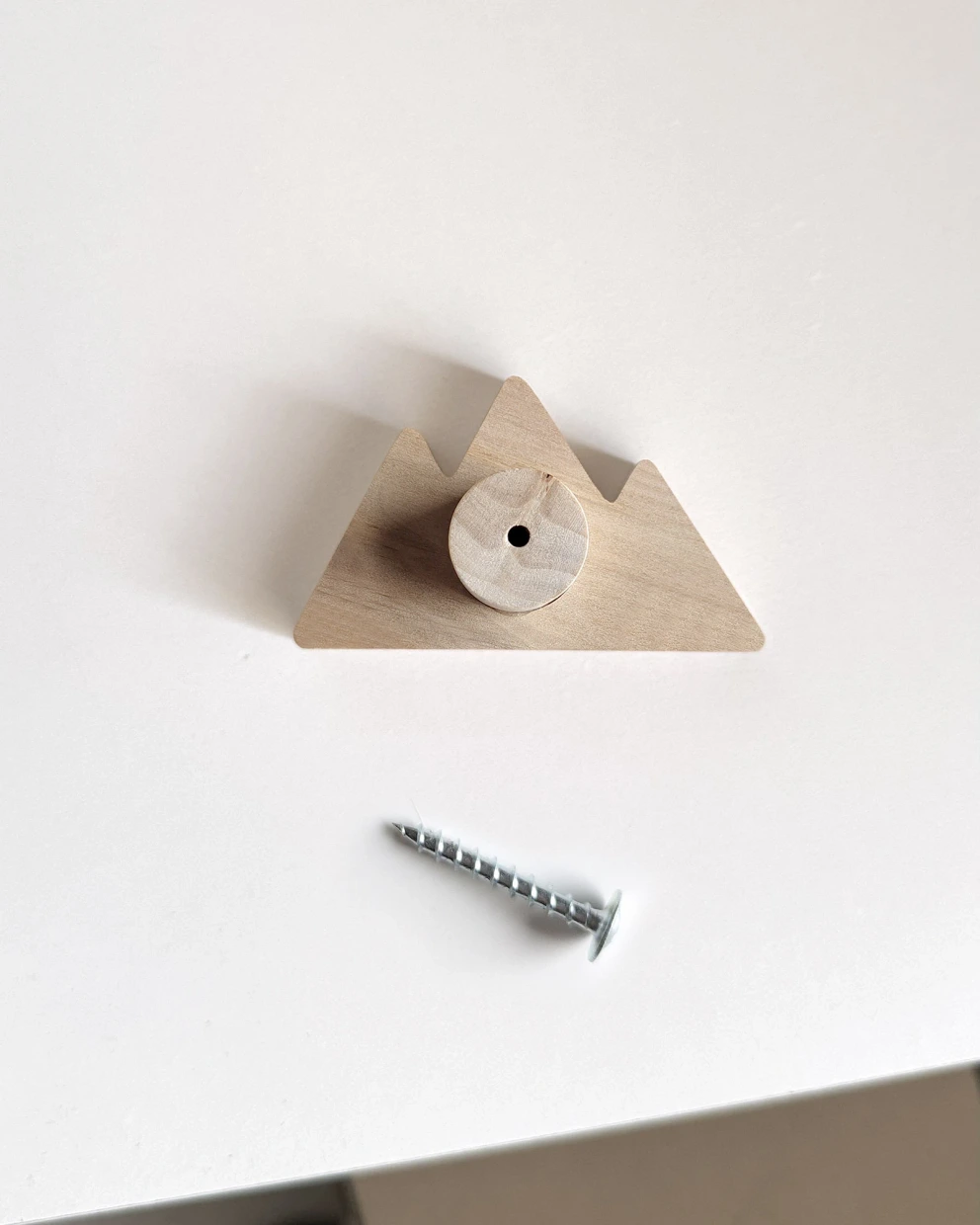 Kalnų formos rankenėlės nugarėlė su montavimo skylute ir komplekte esančiu metaliniu varžtu.