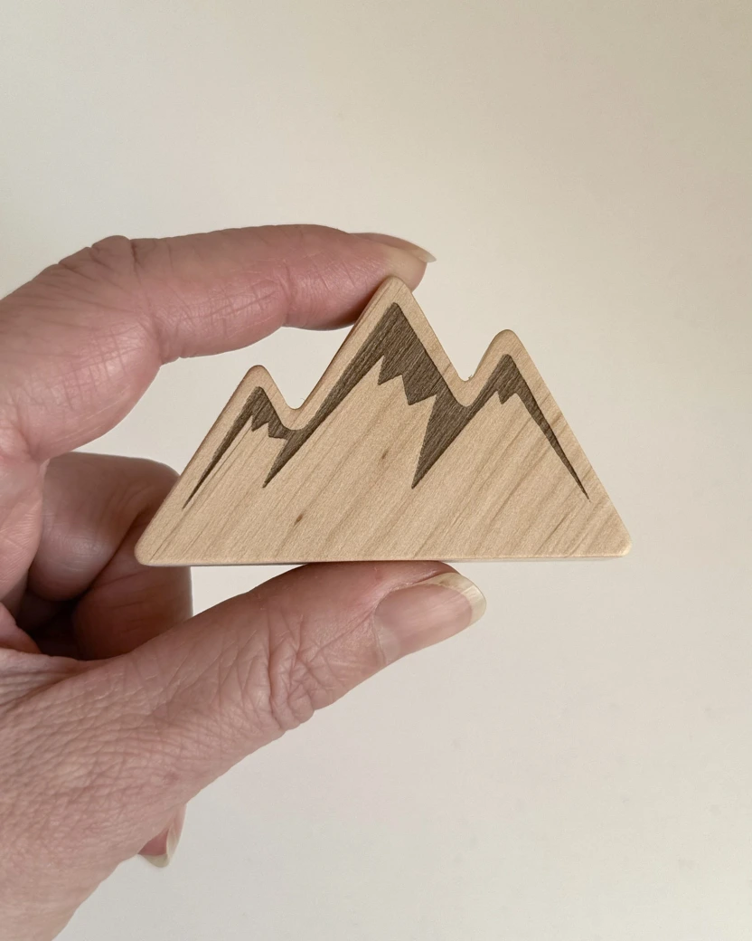 Kalnų formos medinė rankenėlė laikoma rankoje, siekiant parodyti realų gaminio dydį ir mastelį.