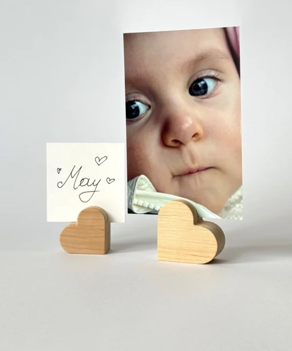 Mažas medinis širdelės formos laikiklis, kuriame įdėta vaiko nuotrauka ir balta kortelė su užrašu May.
