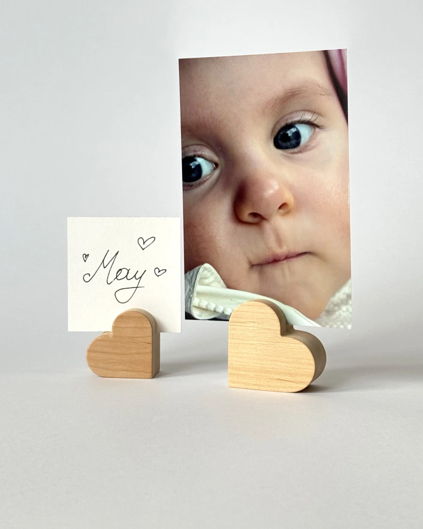 Mažas medinis širdelės formos laikiklis, kuriame įdėta vaiko nuotrauka ir balta kortelė su užrašu May.