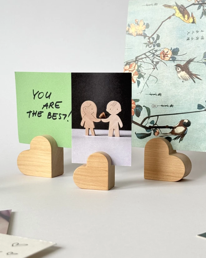 Trys mediniai širdelės formos laikikliai, laikantys žalią raštelį „You are the best“ ir kitus atvirukus.