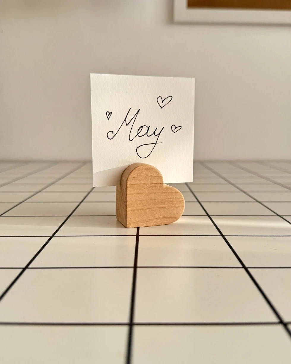 Minimalistinis medinis nuotraukų laikiklis ant languoto stalo su įstatyta balta kortele.