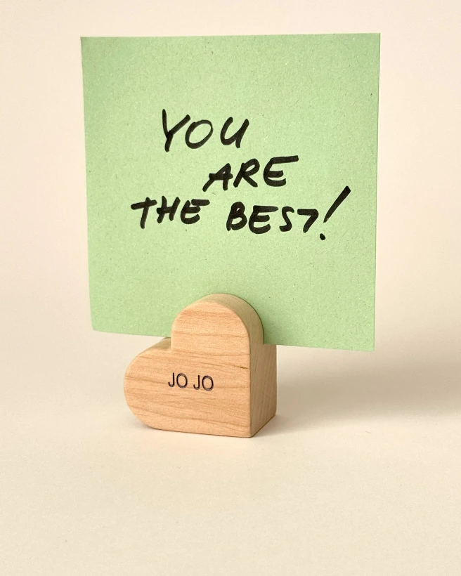 Graviruotas medinis širdelės laikiklis su vardu JO JO, laikantis žalią lapelį su užrašu You are the best.