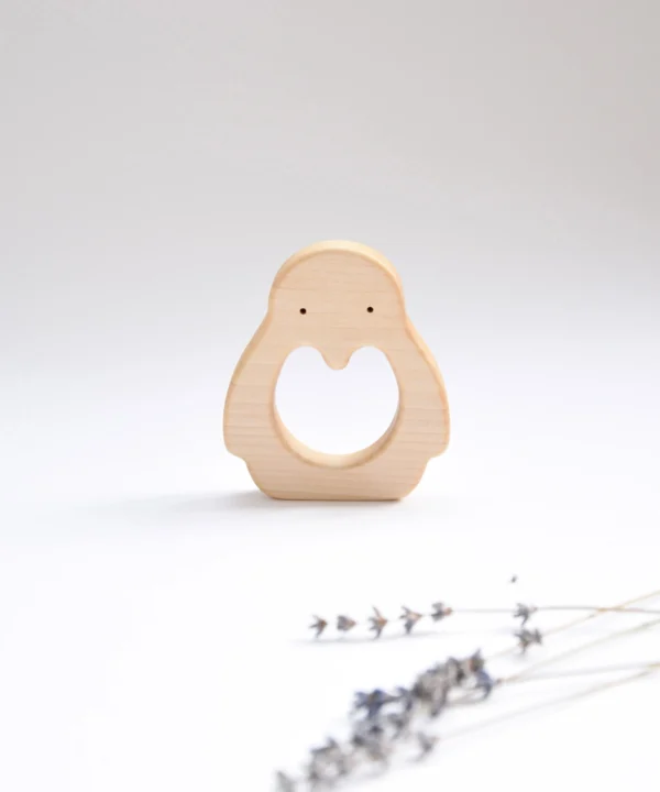 Vertikaliai stovintis medinis pingvino formos kramtukas su dviem taškeliais vietoje akių ir levandų šakele priekyje