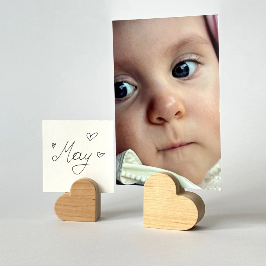 Mažas medinis širdelės formos laikiklis, kuriame įdėta vaiko nuotrauka ir balta kortelė su užrašu May.