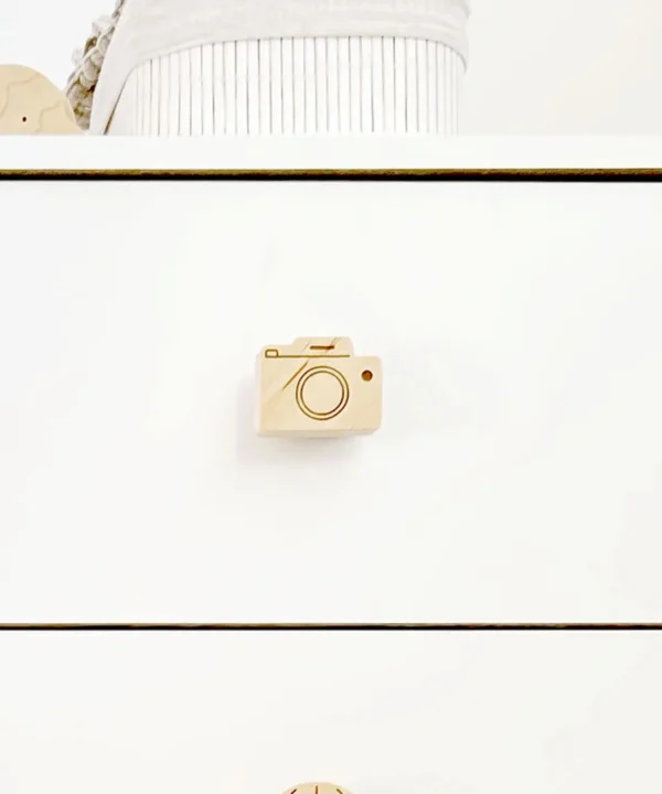 Vaiko kambario komoda su sumontuota medine fotoaparato rankenėle, derinant prie šviesaus skandinaviško stiliaus interjero.