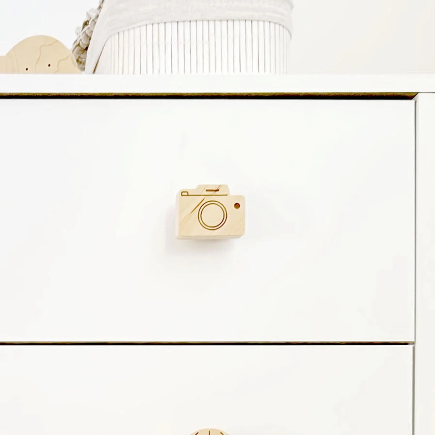 Vaiko kambario komoda su sumontuota medine fotoaparato rankenėle, derinant prie šviesaus skandinaviško stiliaus interjero.