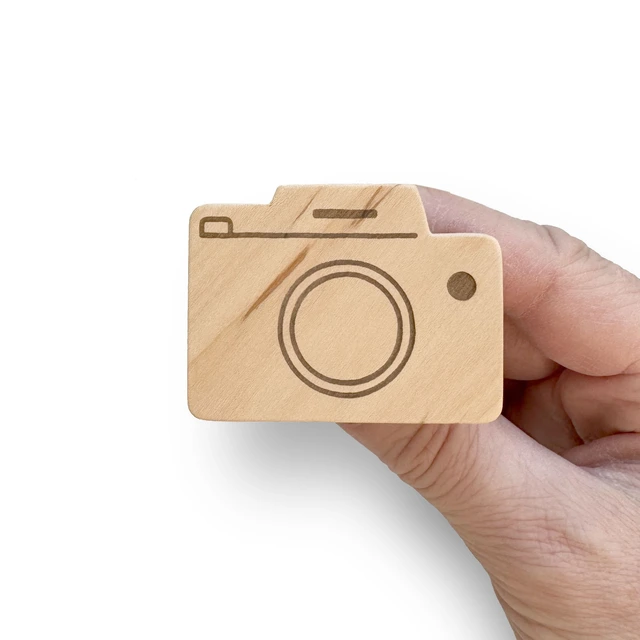 Rankoje laikoma medinė baldų rankenėlė Fotoaparatas, parodanti gaminio dydį, švelniai nušlifuotą paviršių ir lazeriu išgraviruotas detales.